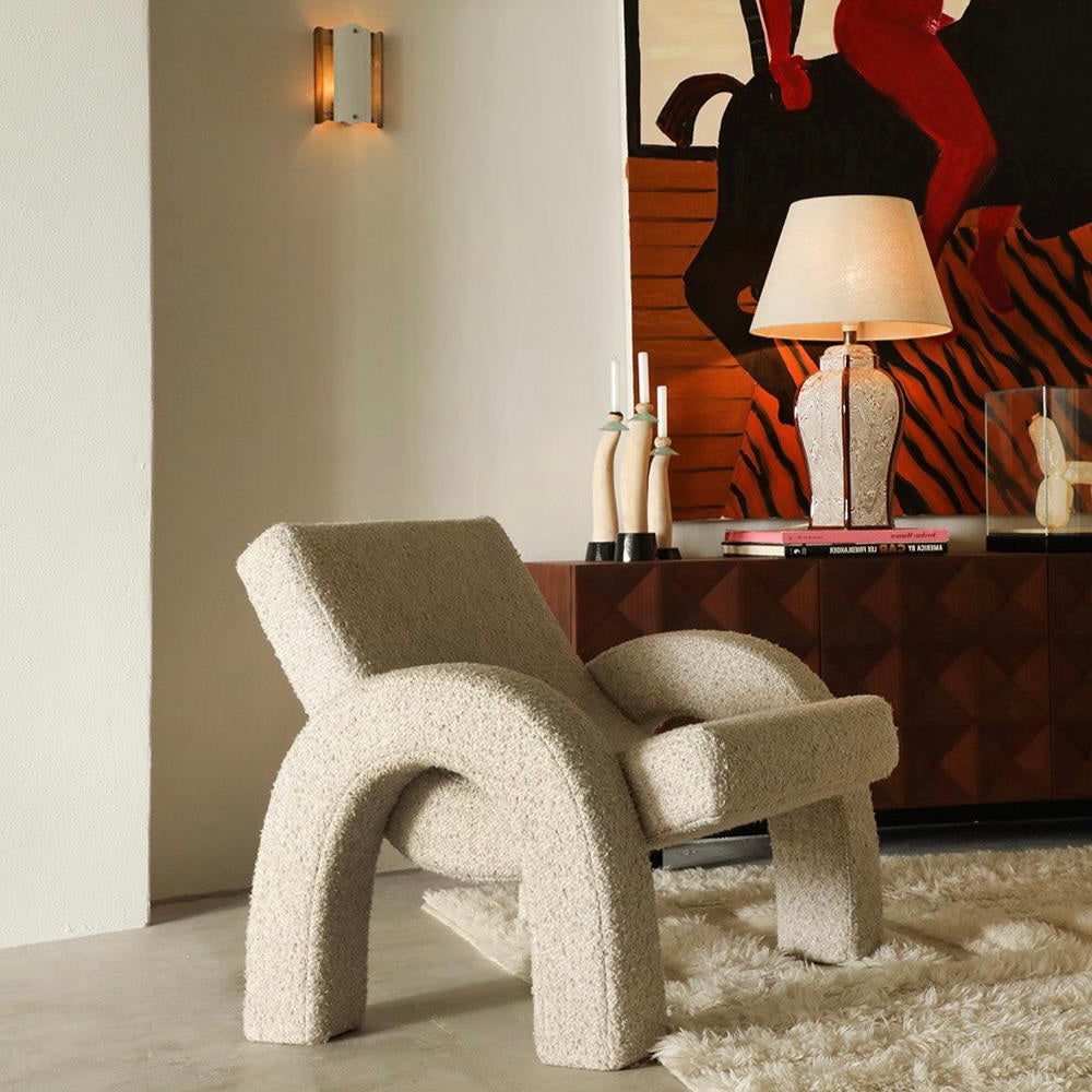 Modern beige armchair in a stylish room with a painting and lamp in the background.