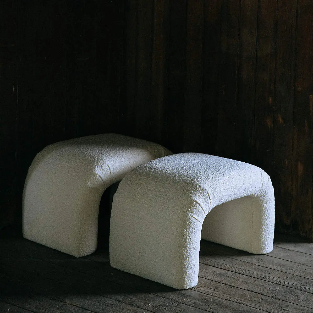 Two white, textured stools on a wooden floor with a dark background