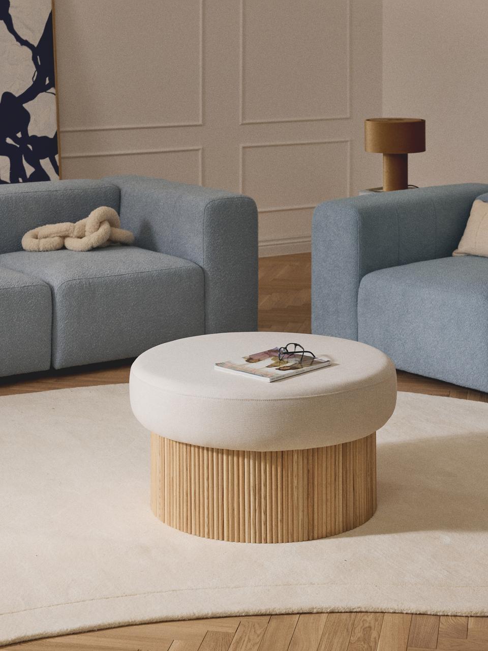 Round ottoman with wooden base and white cushion in a living room setting.