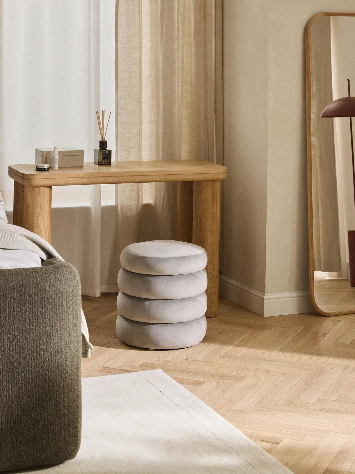 Modern interior with a wooden console table, gray cushioned stool, and large mirror.