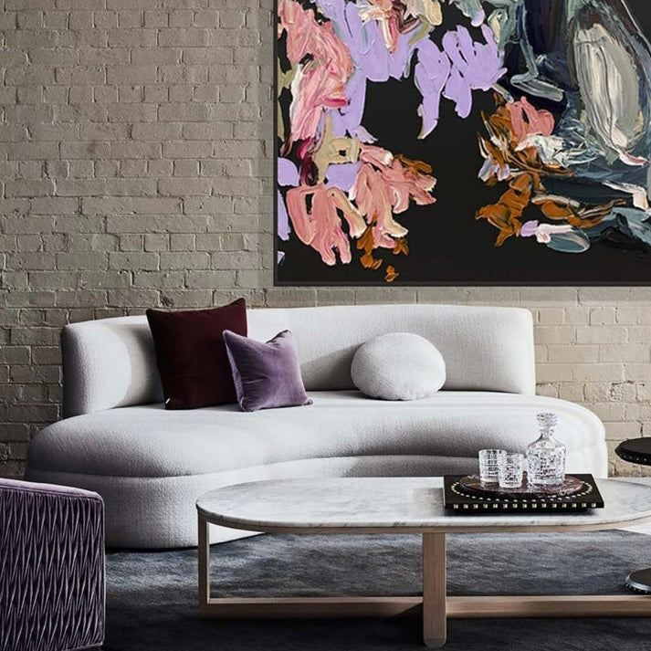 Modern living room with a gray sofa, round coffee table, and colorful abstract painting on a brick wall.