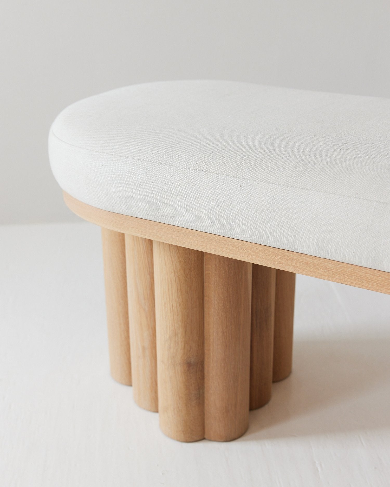 Bench with wooden legs and a white cushion on a light gray background