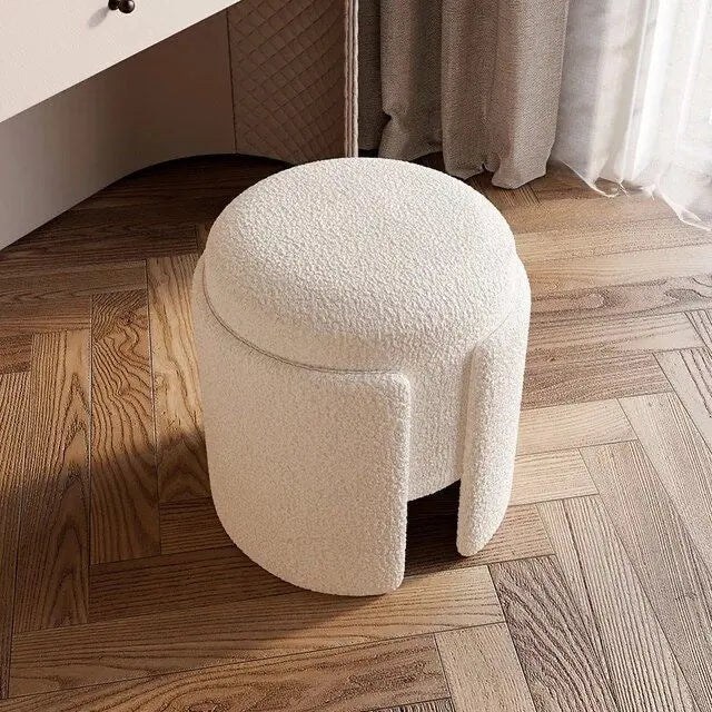 Round textured stool on a wooden floor with curtains in the background