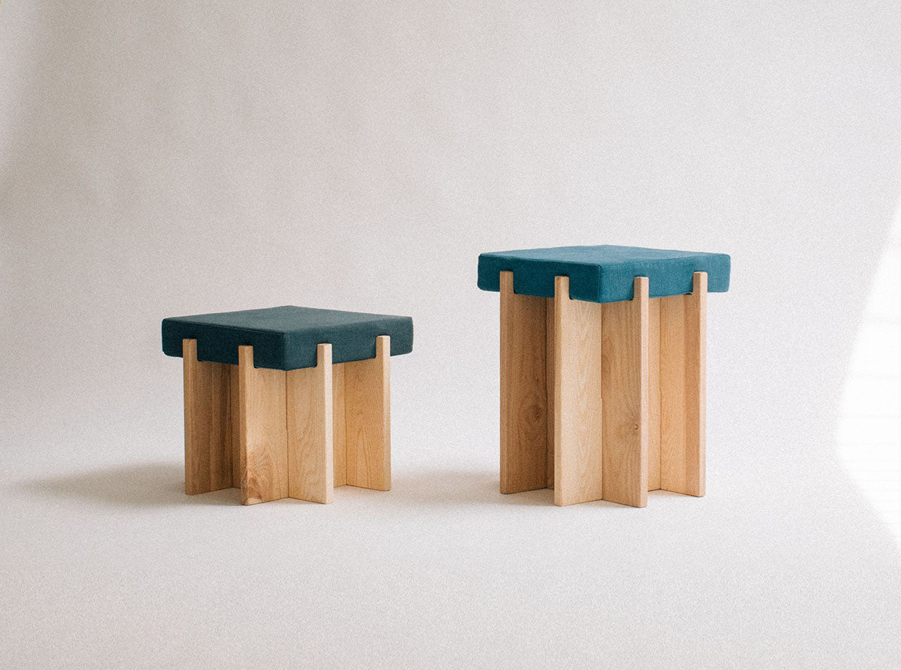 Two stools with teal seats and wooden legs on a light background