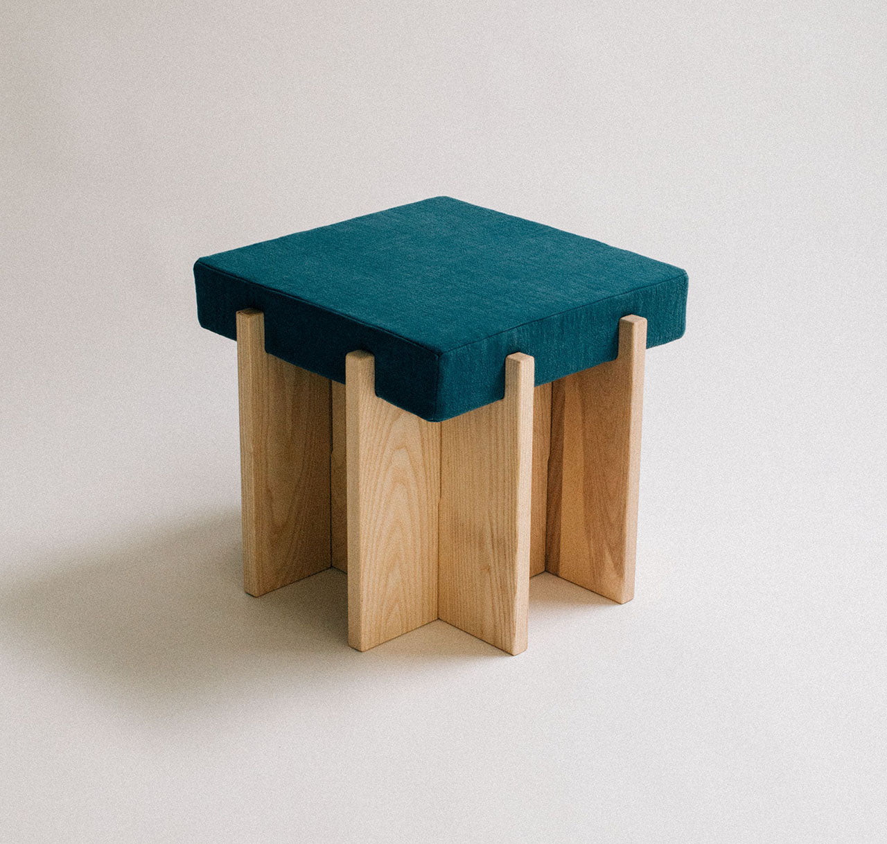 Small stool with teal cushioned top and wooden legs on a plain background