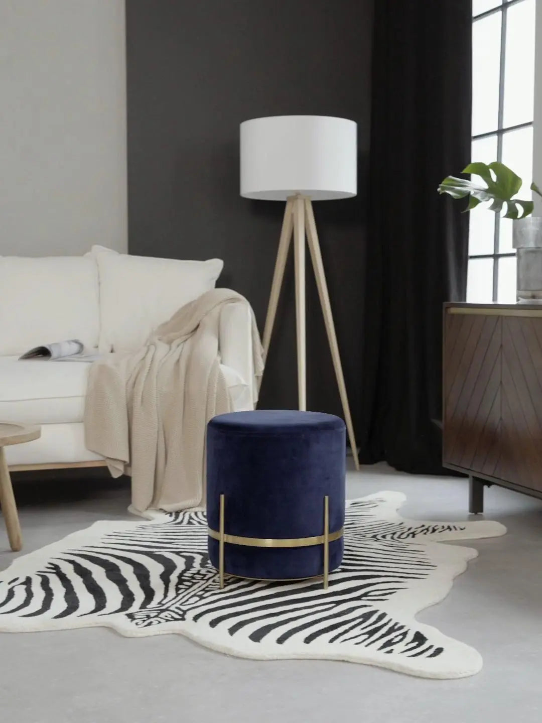 Navy blue ottoman with gold legs on a zebra print rug in a living room setting.