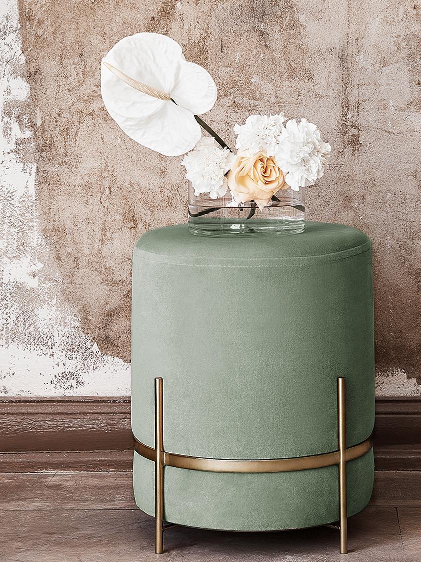 Green side table with gold legs holding a vase of flowers against a textured wall.