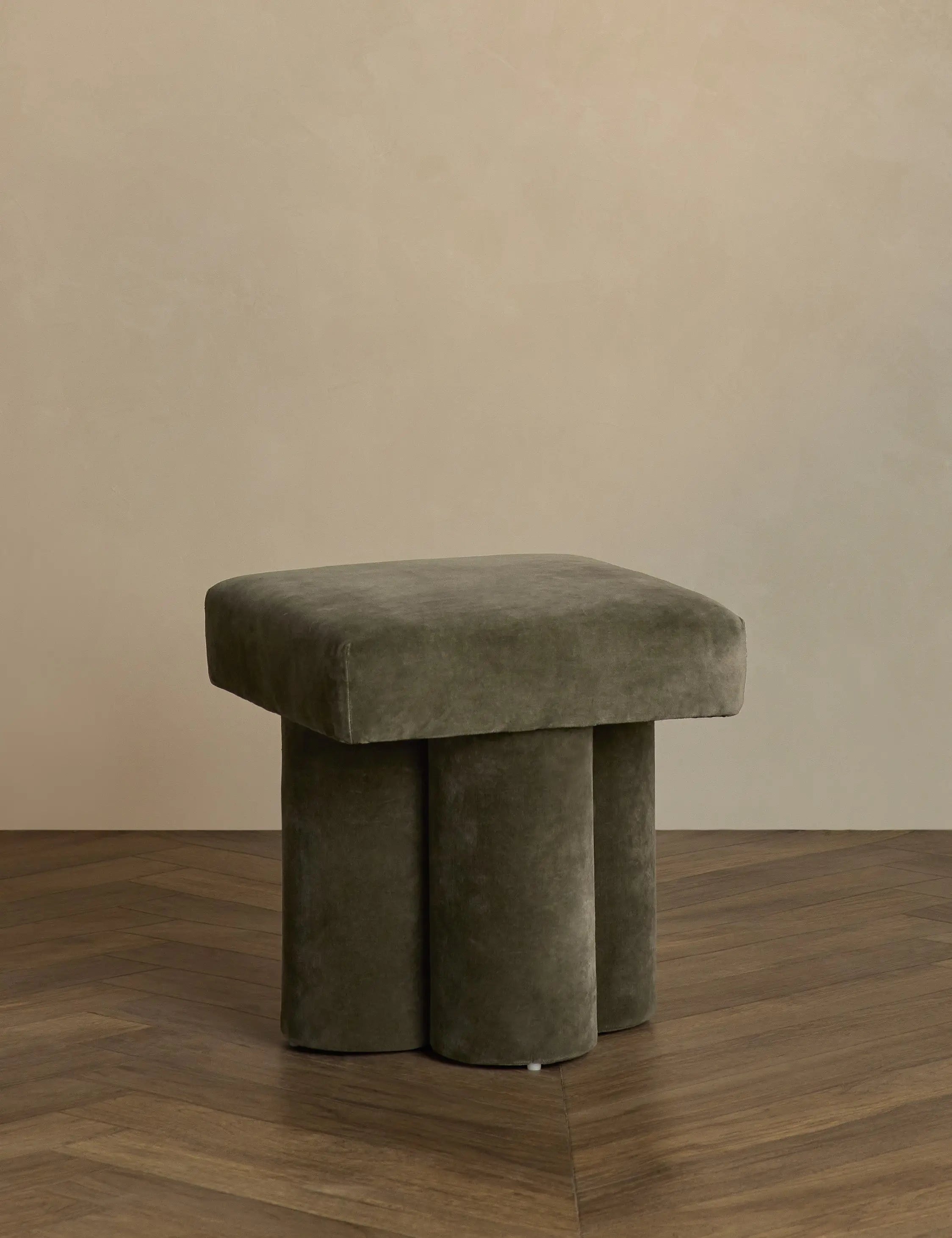 Olive cushioned stool on a wooden floor with a beige wall background