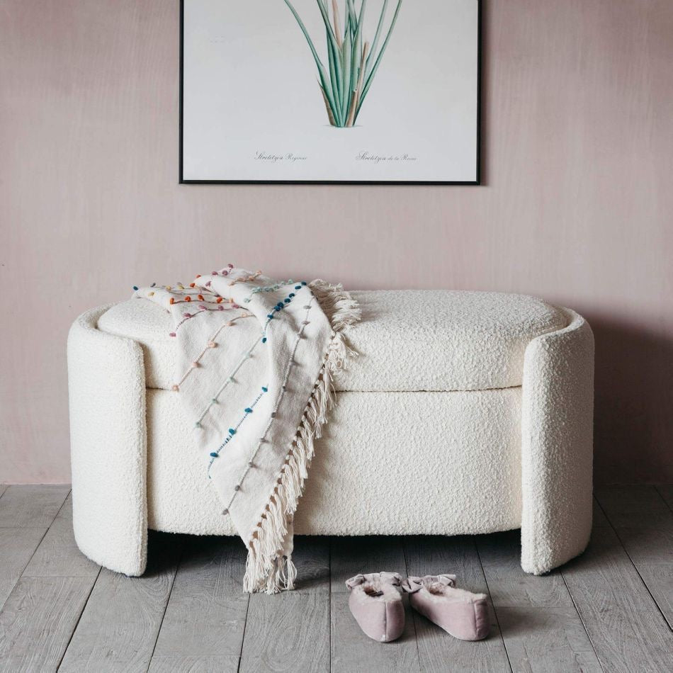 White textured Bench with a blanket and shoes on a wooden floor against a pink wall with a framed picture.