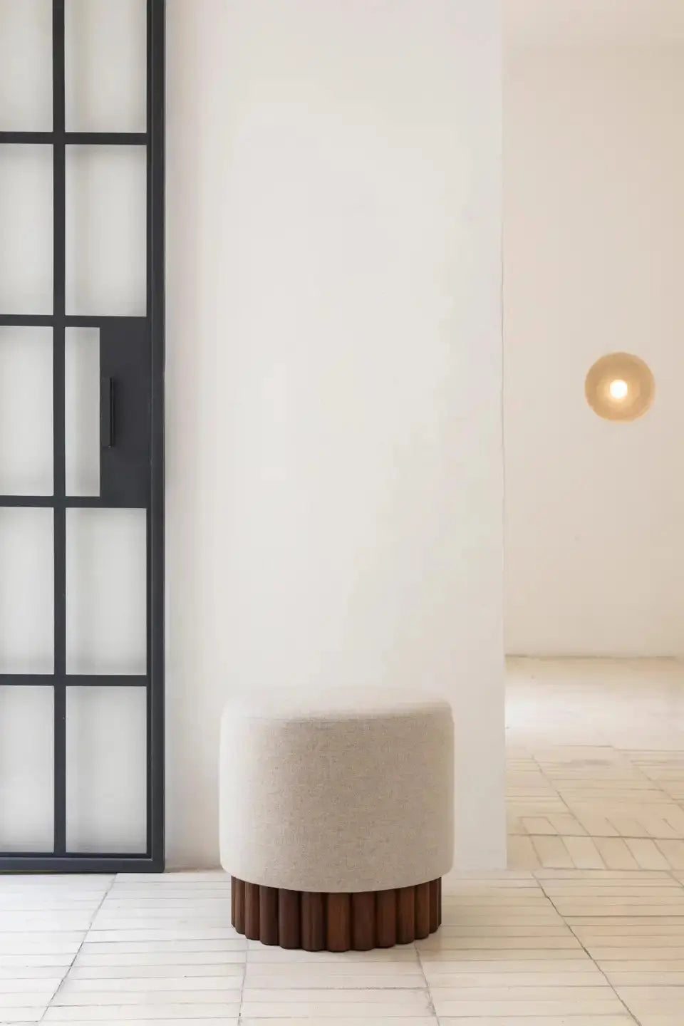 White cylindrical ottoman with wooden base against a light-colored wall.