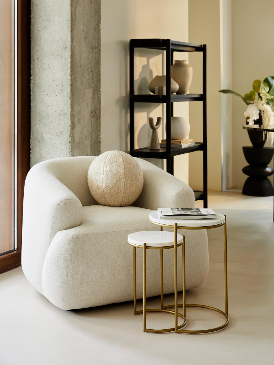 Modern living room with a white armchair, gold side table, and decorative shelves.