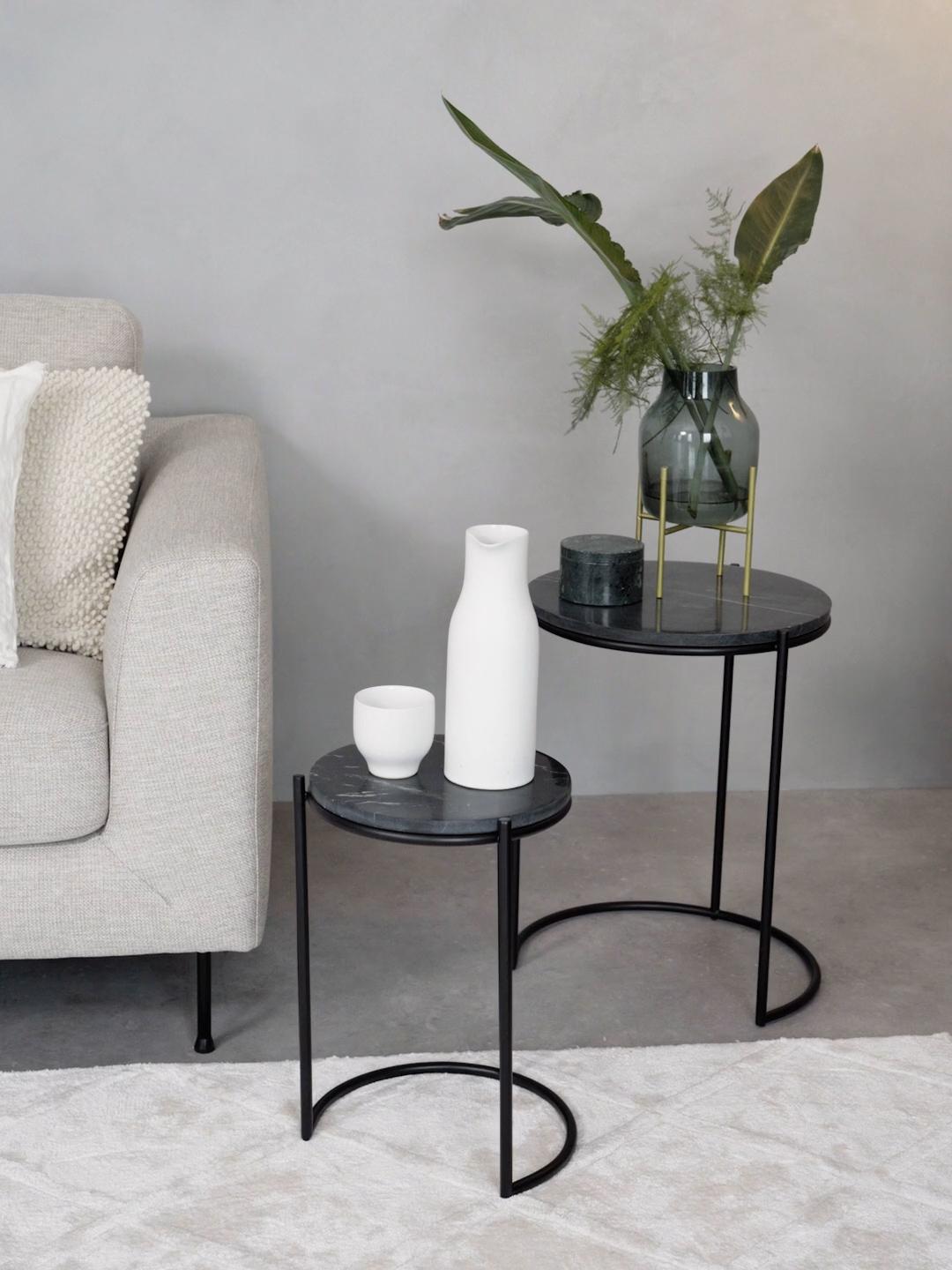 Two black marble side tables with decorative items in a living room setting.