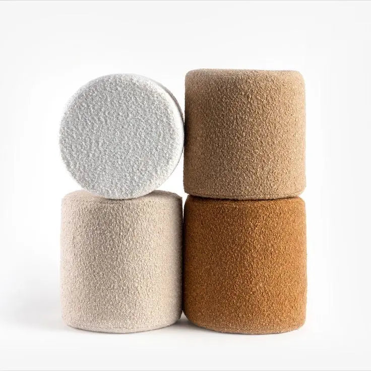 Four cylindrical ottomans in different colors stacked on a white background