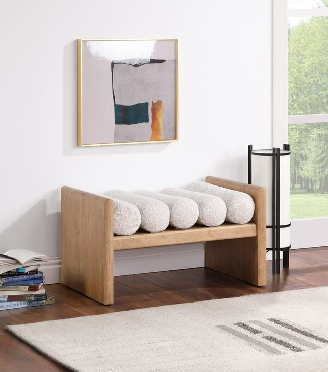 Wooden bench with white cushions in a room with a painting on the wall and books on the floor.