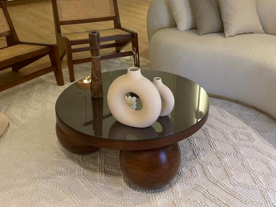 Round wooden coffee table with two white vases in a living room setting.