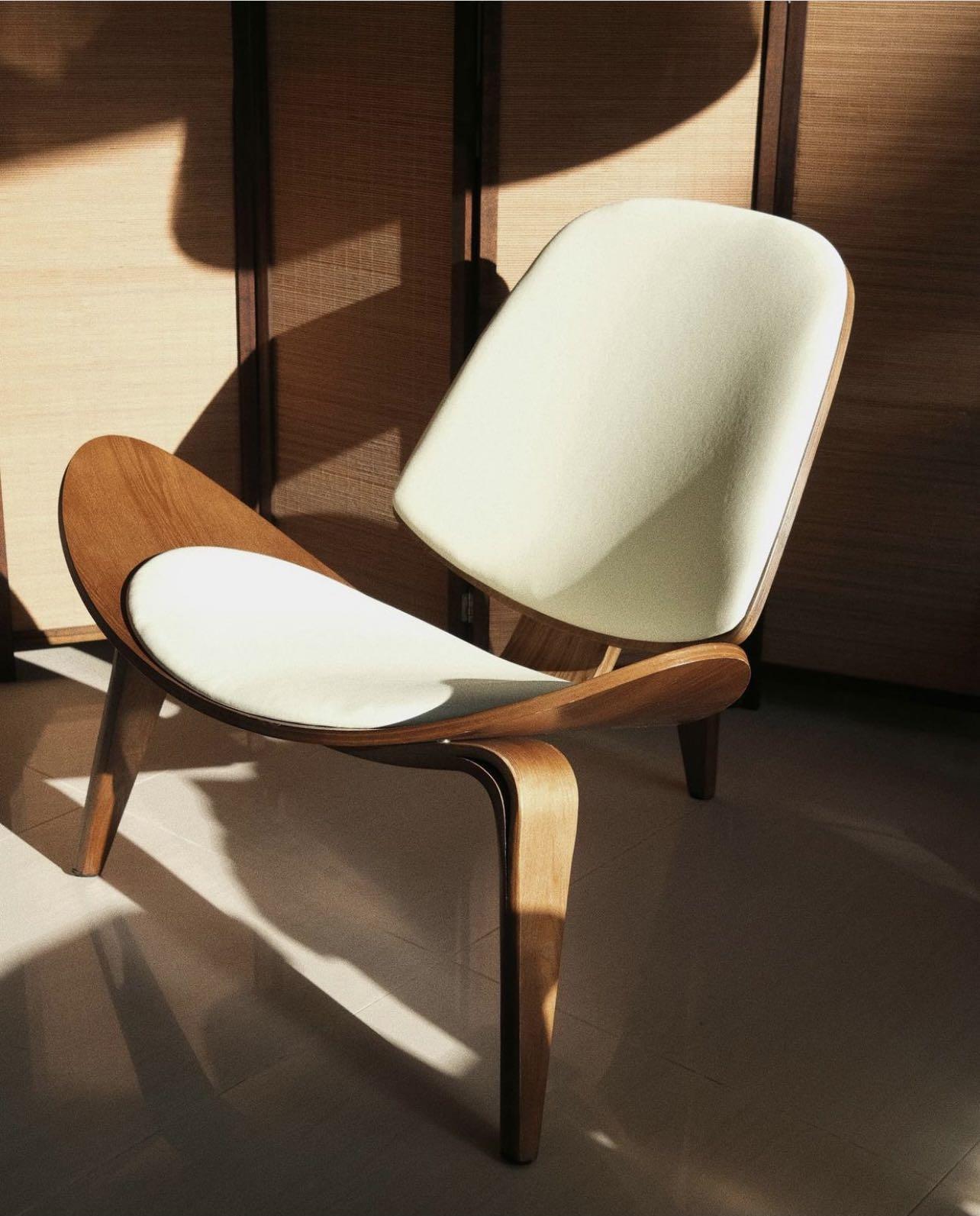 Modern chair with wooden frame and white seat and backrest in a softly lit room.