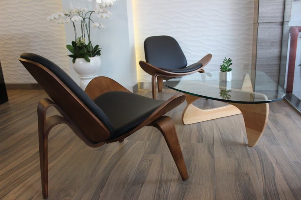Modern lounge chair and glass table in a room with wooden flooring and plants.